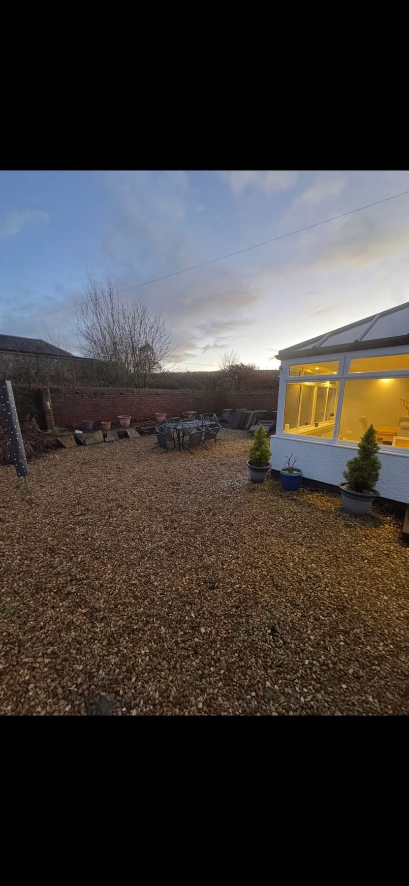 Before — original gravel yard at dusk with conservatory and brick walls