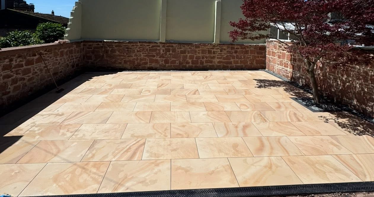 Close-up of the rippled buff sandstone paving laid in a stack-bond pattern with a channel drain along the front edge