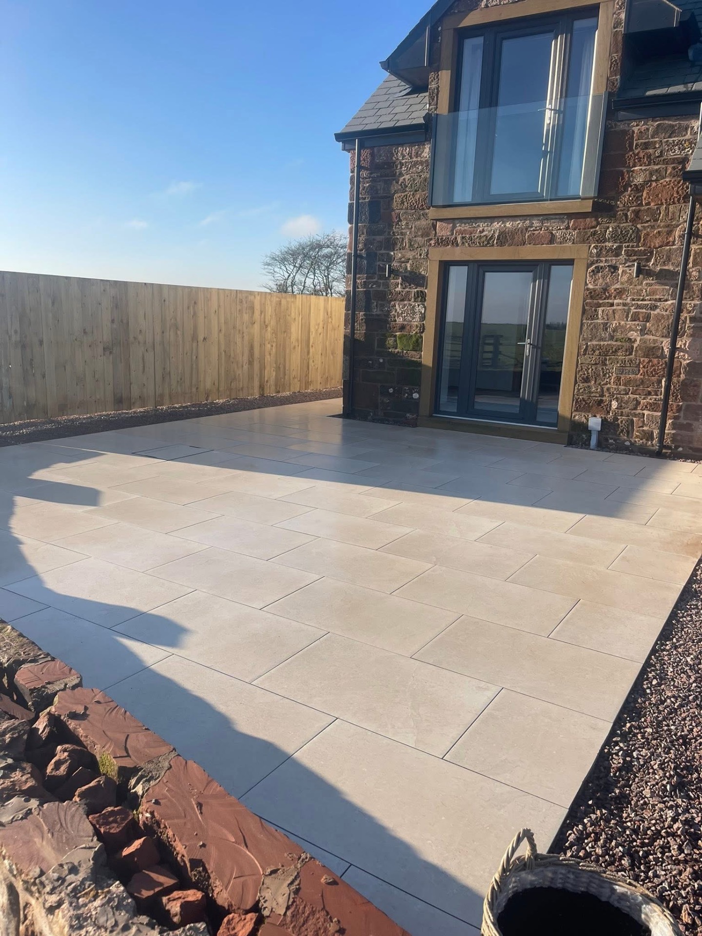 After — gable end of the stone farmhouse with porcelain paving wrapping past the bay window to a timber boundary fence
