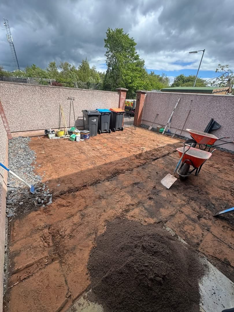 Before — stripped-out walled courtyard with bare sub-base, wheelbarrows and tools on site ready for porcelain paving